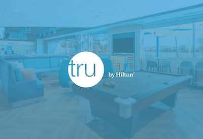 A hotel communal area with the Tru by Hilton logo layered over the top